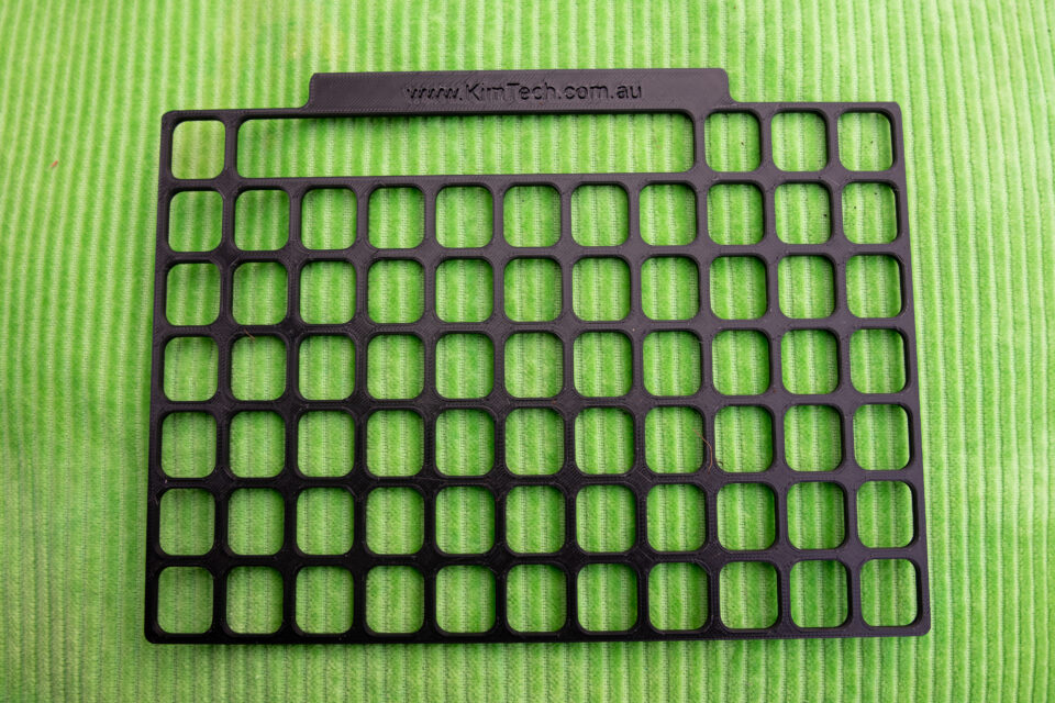 A black 3D printed keyguard for TD Snap Motor Plan 66 displayed on a green cushion.